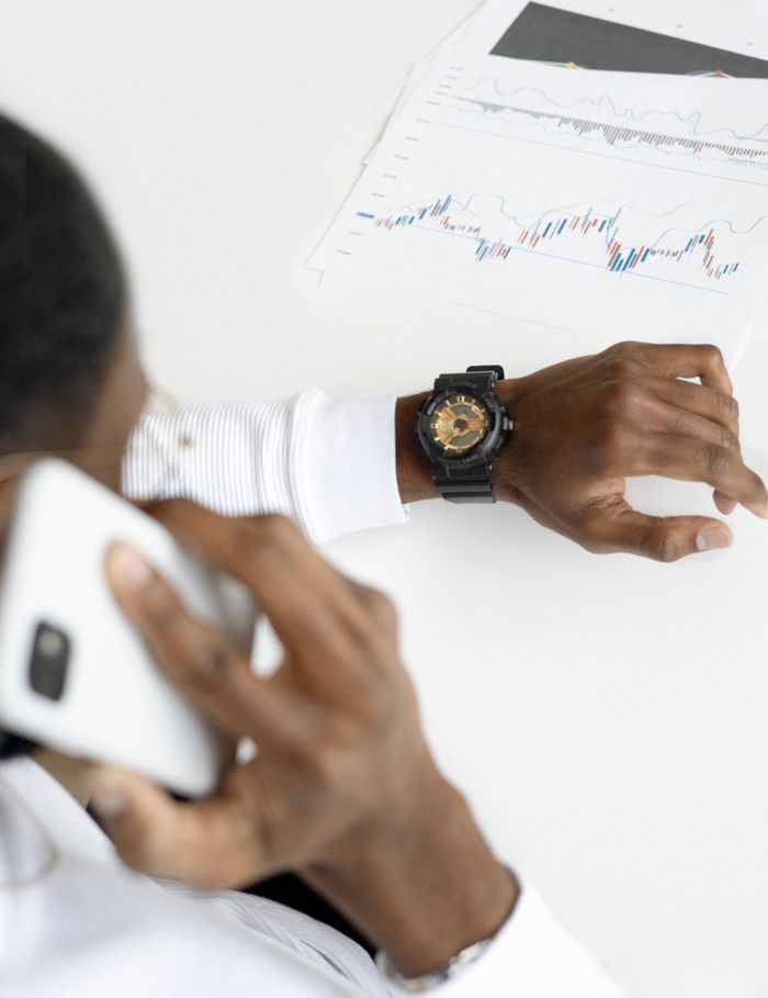 services-03 Man examining financial charts on paper while talking on smartphone in office setting.